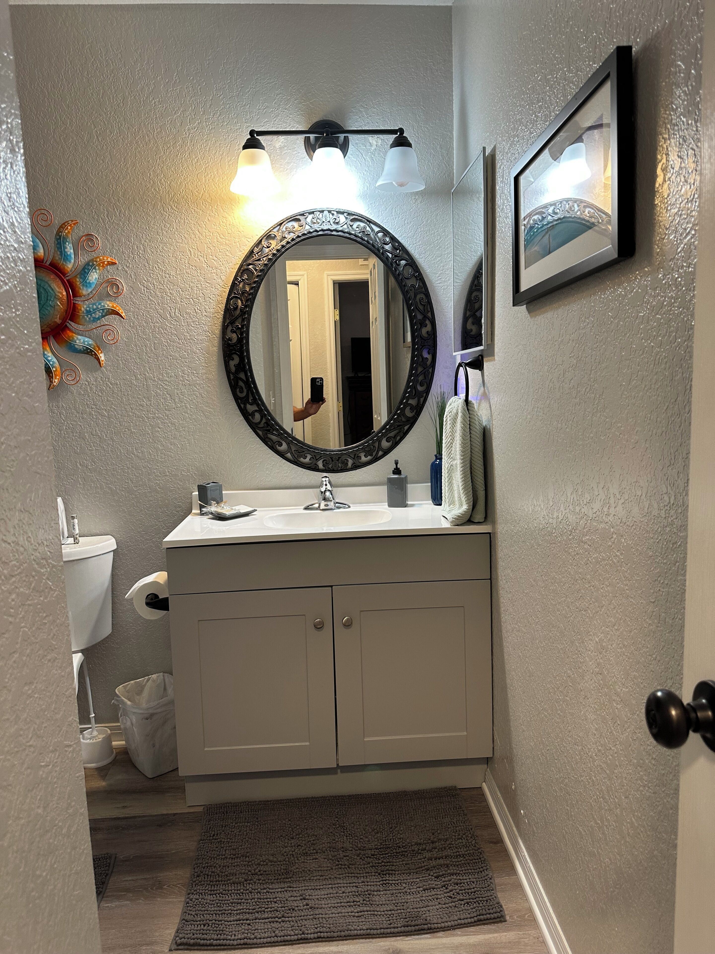 A bathroom with a white sink, a round mirror with a black frame, and a light fixture above the mirror.