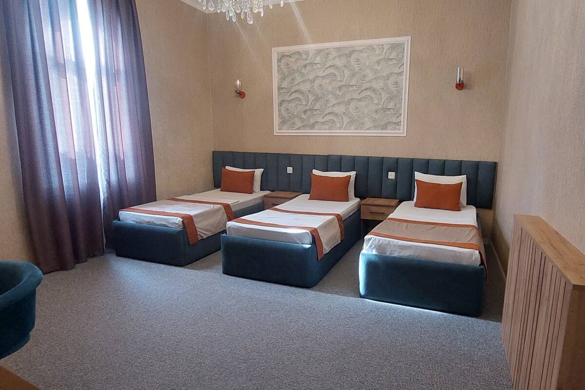 A hotel room with three beds, a wooden desk, a blue chair, and a chandelier.