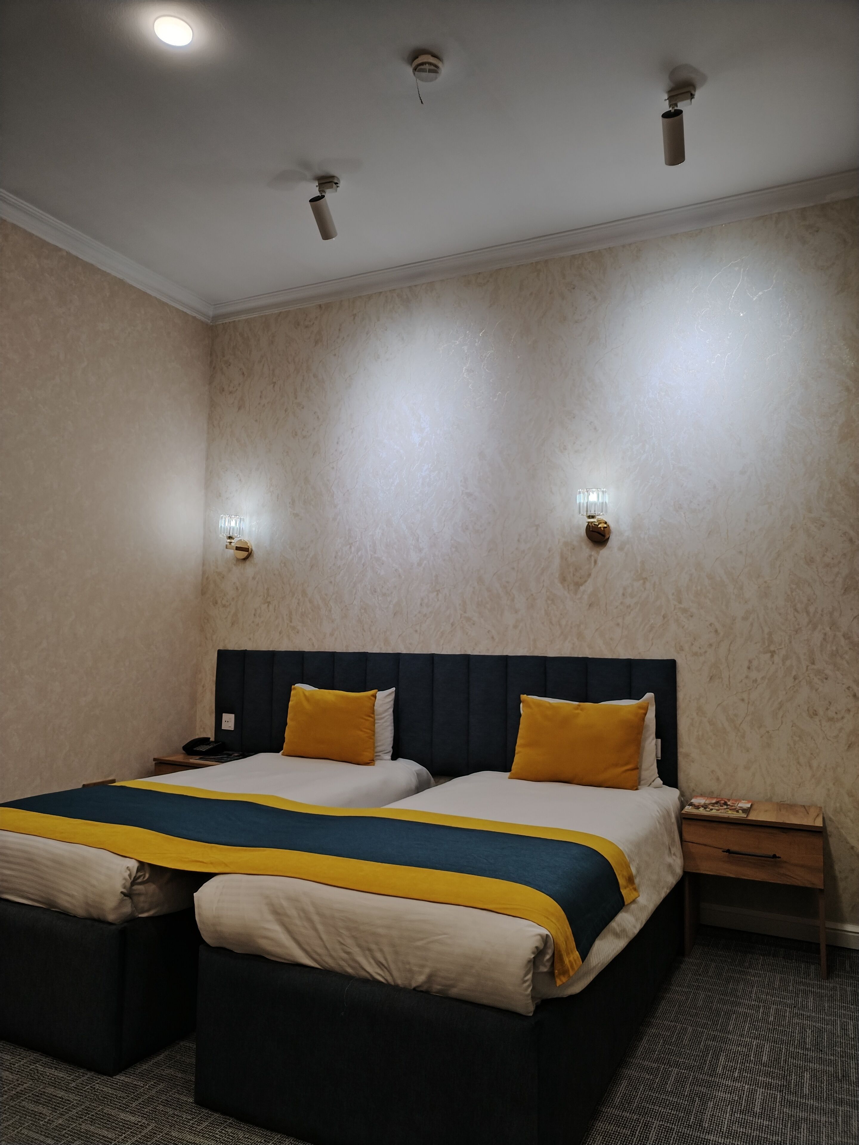 Une chambre d’hôtel avec un grand lit, deux tables de chevet, une petite table et une lampe fixée au mur.