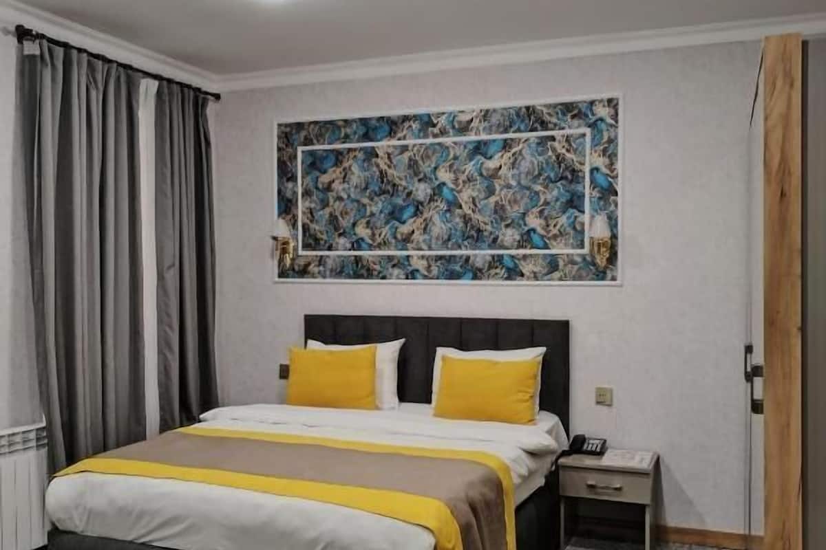 A hotel room with a bed, a nightstand, a telephone, and a painting on the wall.