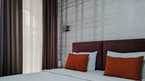 Een hotelkamer met een groot bed, twee kussens, een hoofdeinde en een raam met gordijnen.
