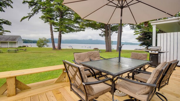 Een terras buiten met een tafel en stoelen, een barbecue en uitzicht op een meer met boten.