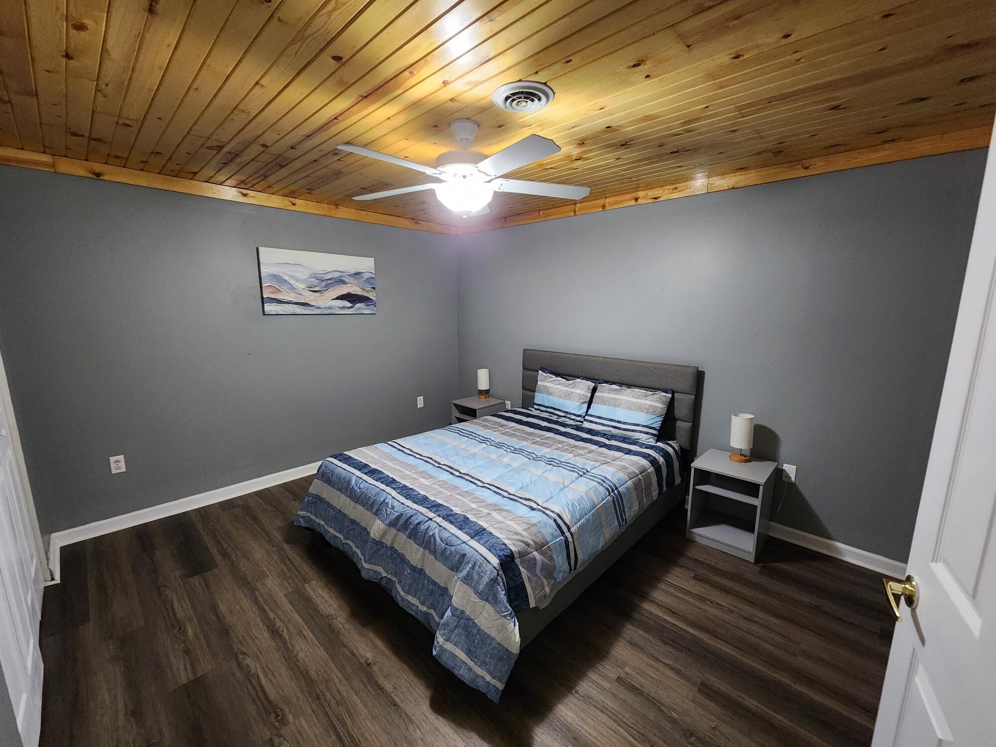 Une chambre à coucher comprenant un lit, un ventilateur de plafond, une table de chevet et une lampe fixée au mur.