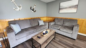 A living room with two grey sofas, a coffee table, and wooden paneling on the walls.