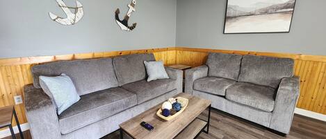 Ein Wohnzimmer mit zwei grauen Sofas, einem Couchtisch und Holzvertäfelung an den Wänden.