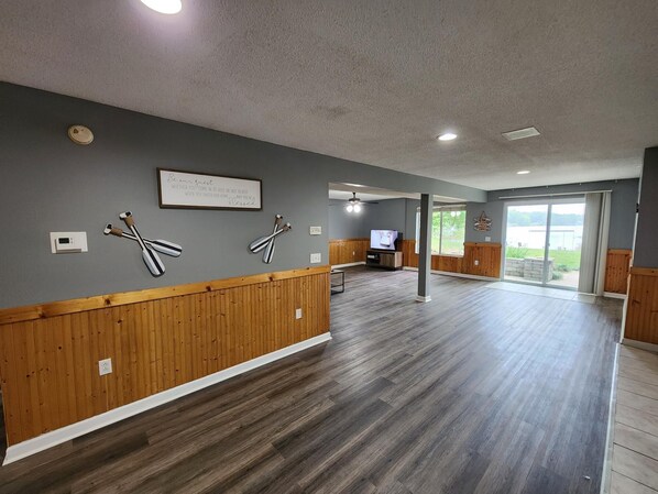 A spacious room with wooden paneling, a flat-screen TV, and a large sliding glass door leading to an outdoor area.