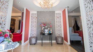 A hotel lobby with a chandelier, a red chair, a blue chair, and a table with a clock and flowers. - The star of sathon Luxury king room 502 (Krung Thep Maha Nakhon)