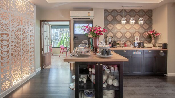 A modern kitchen with a central island, dark cabinetry, decorative wall patterns, and a view of the outdoor area. - The star of sathon Luxury king room 502 (Krung Thep Maha Nakhon)