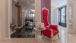 A spacious room with a red upholstered chair, a small table with a decorative item, and a view of a hallway with a decorative wall panel. - The star of sathon Luxury king room 502 (Krung Thep Maha Nakhon)