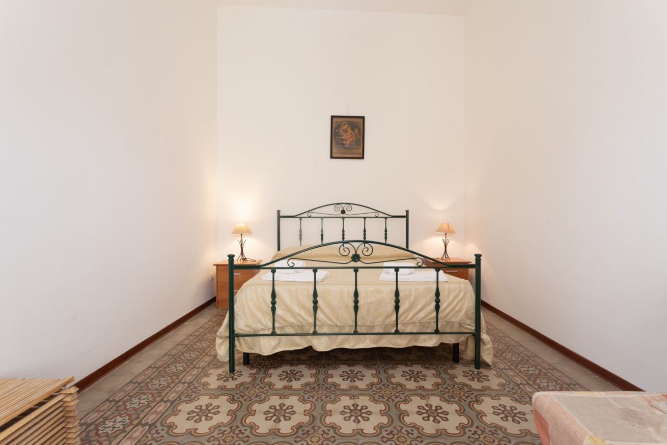 Quarto com cama, duas luminárias de cabeceira, uma mesinha e piso estampado.