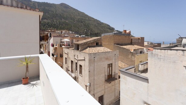 A residential area with terracotta-roofed buildings, a potted plant on a balcony, and a mountainous backdrop. - GuestHost - Castellammare Stella Apartment with Terrace (Castellammare del Golfo)