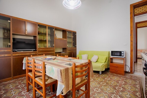 A dining area with a table set for four, surrounded by wooden chairs. A television is mounted on the wall above the table.
