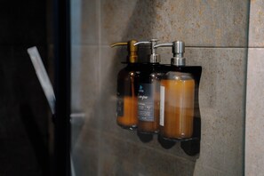 A bathroom with a glass shower enclosure and two bottles of shampoo on a tiled wall. - (Casablanca)