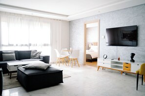 Ein modernes Wohnzimmer mit einer Couch, einem Hocker und einem an der Wand montierten Fernseher.
