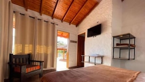 A bedroom with a wooden ceiling, a bed, a chair, a TV mounted on the wall, and a small table. - Finca-hotel Montecarlo by Hope (Antioquia)