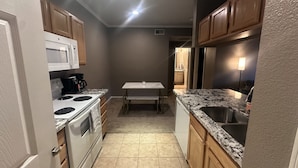 A compact kitchen with a white stove, microwave, and refrigerator, wooden cabinets, and a marble countertop.