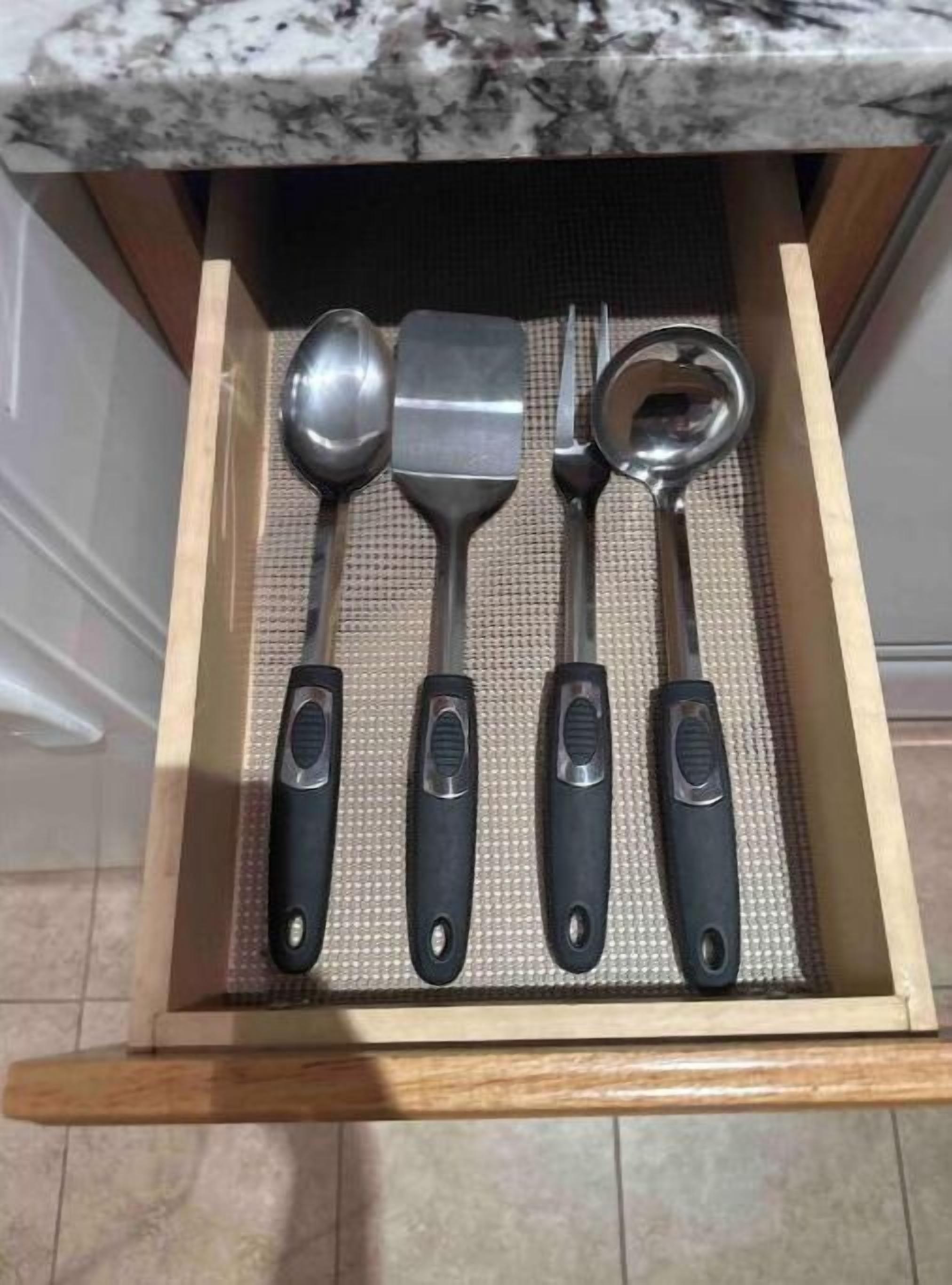 A drawer containing a spatula, a ladle, a spoon, and a fork with black handles.
