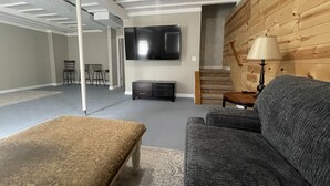 A modern living room with a grey sofa, a patterned ottoman, a flat-screen TV, and a wooden accent wall. - Peaceful Hideaway! New Listing (Roscommon)
