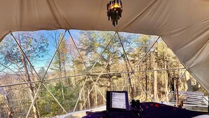 Eine Zeltdomizil mit einem Bett, einem festmontierten Computer und Blick auf den Wald.
