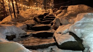 Schneebedeckte Felsen und verschneite Landschaft bei Nacht, beleuchtet durch Lichterketten.