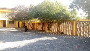 Un camino de grava que conduce a un edificio con fachada amarilla y una valla enrejada.