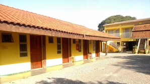 Un edificio amarillo con techo de tejas rojas, un patio de grava y una escalera que conduce a un nivel superior.