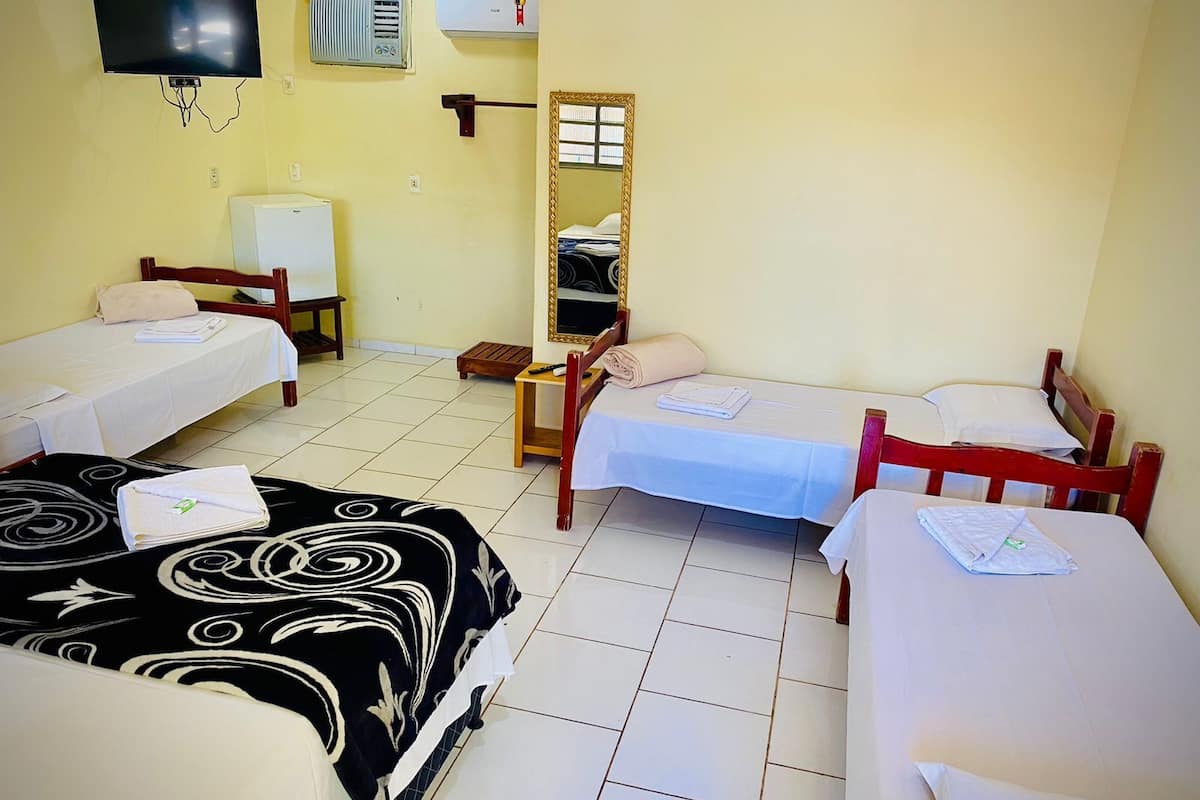 A hotel room with two single beds, a television, an air conditioner, and a mirror.