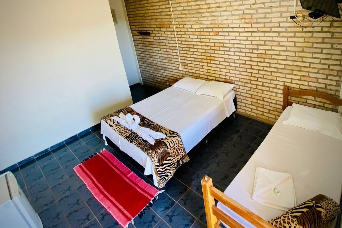 A single bed with a zebra-patterned blanket and a red throw, a wooden chair, and a brick-patterned wall.