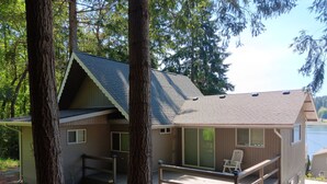 Une cabane dotée d’une terrasse, entourée d’arbres et située près d’un plan d’eau.