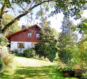 A red wooden house with a white facade, surrounded by lush greenery and a well-maintained garden.