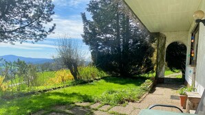 A patio with a table and chairs, surrounded by a garden with a view of distant hills.