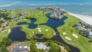 An aerial view of a golf course with a water feature, surrounded by residential buildings and a beach. - Renovated Center Island Home & Garage Apt 4bd/3ba (Fripp Island)