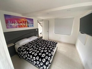 Une chambre à coucher avec un lit, un tableau au mur, une télévision et une porte.