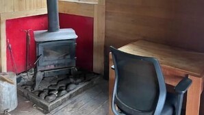 A rustic cabin with a wood-burning stove, a single window, and a chair.