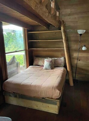 Relax in a serene bedroom with a sloped ceiling offering a view of the outdoors, featuring a simple bed and a bedside lamp.