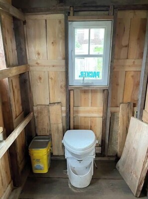 A compact space with a window offering a view of the surrounding greenery, featuring a toilet and storage options.