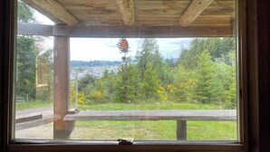 A wooden structure with a large window overlooking a green landscape and a distant town.