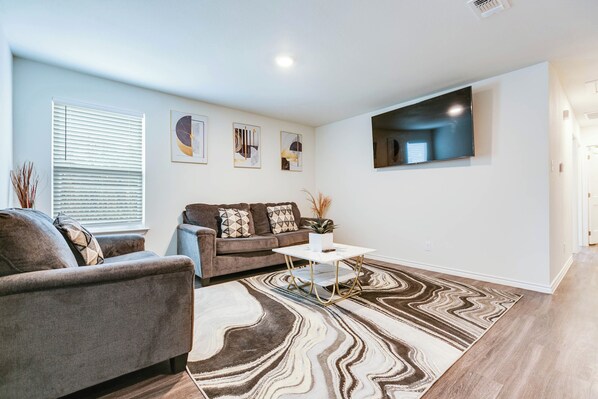 A living room with a sofa, a coffee table, and a TV mounted on the wall. - 3BR Moments from Goodfellow AFB! (San Angelo)