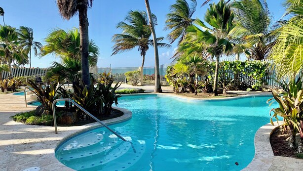 A swimming pool with a tiled deck, surrounded by palm trees and a white fence. - Paradise in Rio Grande, Puerto Rico Right Next door to Four Seasons (Río Grande)