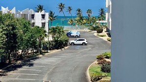A street with a white car parked on the side, palm trees, and a building with a white facade. - Paradise in Rio Grande, Puerto Rico Right Next door to Four Seasons (Río Grande)