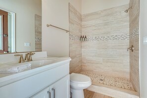 Een badkamer met een wit wastafel, een gouden kraan en een wit toilet. Er is een douche met beige tegels en een klein plankje met toiletartikelen.