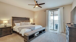 Een slaapkamer met een bed, nachtkastjes, een bankje, een plafondventilator en uitzicht door een schuifdeur.