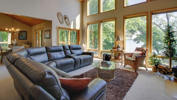 Ein geräumiges Wohnzimmer mit einem Ledersofa, einem Glastisch und einem großen Fenster mit Blick auf einen Wald.