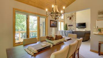 A dining area with a wooden table, chairs, a chandelier, and a television in the background.