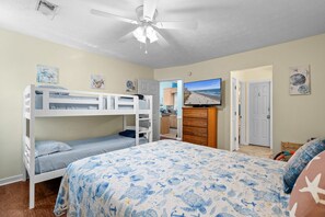 Une chambre avec des lits superposés, un ventilateur de plafond, une télévision et des œuvres d’art sur le thème de la marine.