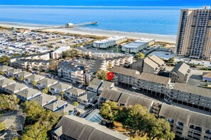 Vue aérienne d’un quartier résidentiel situé sur la côte, avec de nombreux immeubles d’appartements, une jetée qui s’avance dans l’océan et un grand hôtel reconnaissable à son toit rouge.