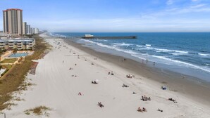 A beach with a long pier extending into the ocean, surrounded by high-rise buildings.