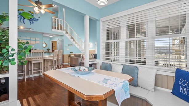 A spacious living area with a wooden dining table, a staircase, and a large window with blinds.