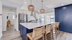 A modern kitchen with a large island, stainless steel appliances, and wicker pendant lights. - 530 Coastal Cabana – Waterfront Pool Home w/ Hot Tub, Dock, Golf Cart & Walk to Beach (Indian Rocks Beach)