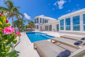 Una casa moderna de dos pisos con piscina, mobiliario exterior y palmeras.